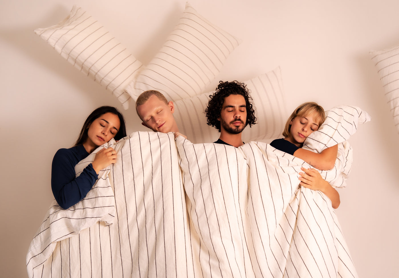 Couple in navy pinstripe Zed Sleep pyjamas resting in bed under a white duvet, premium-mood lifestyle shot