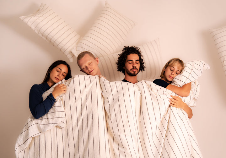 Couple in navy pinstripe Zed Sleep pyjamas resting in bed under a white duvet, premium-mood lifestyle shot