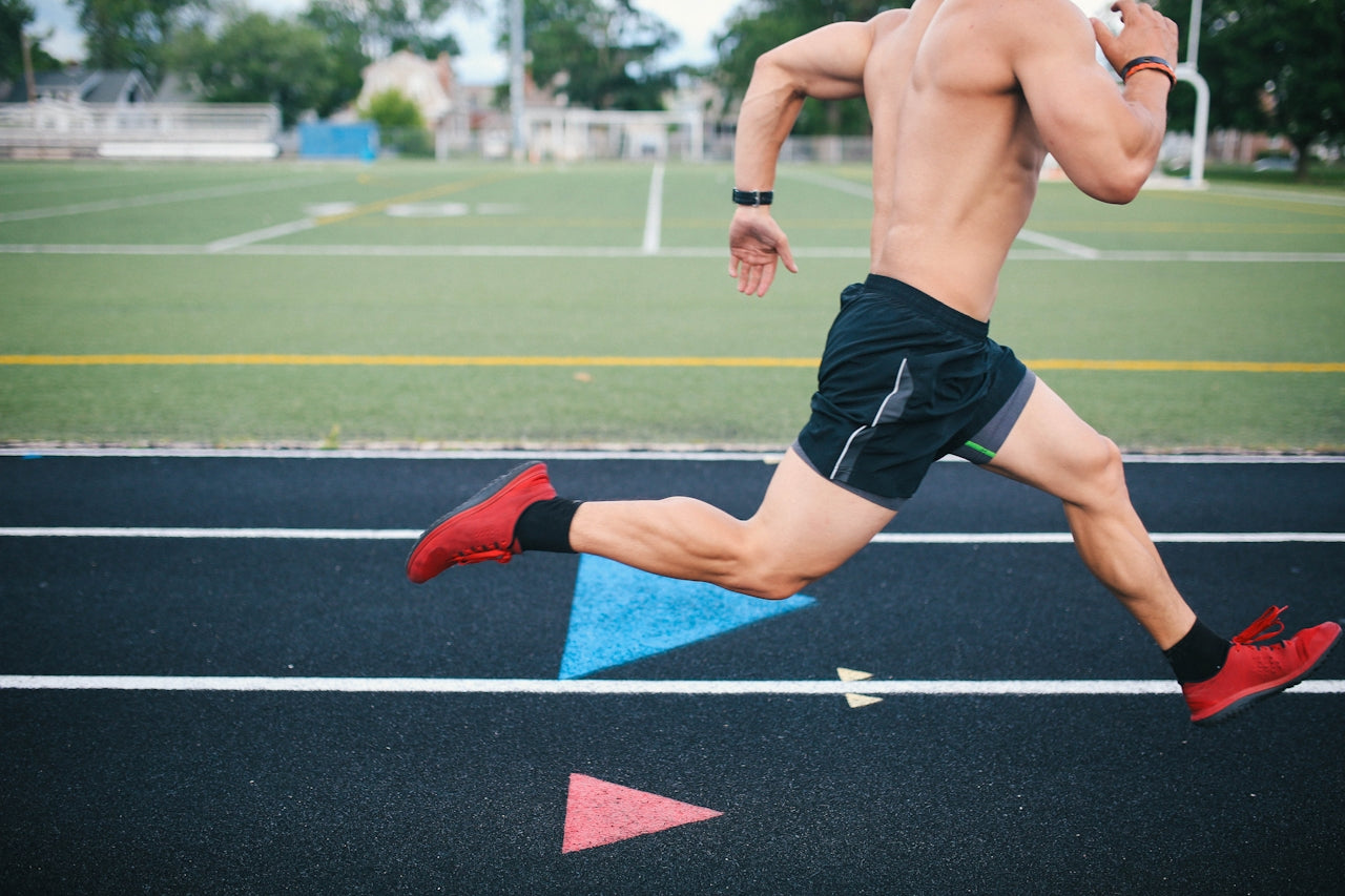 Male athlete mid-stride on a running track adjacent to a football pitch, recovery and training environment