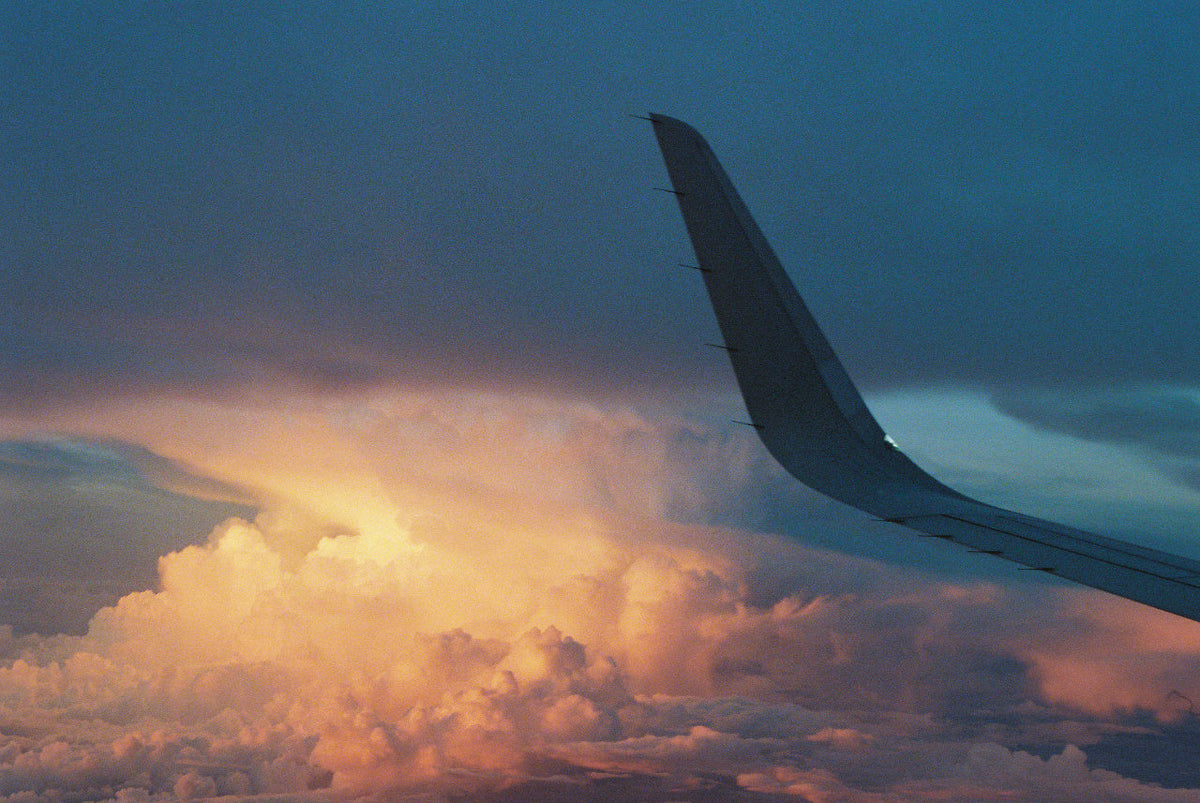 An airplane wing against glowing sunset clouds, seen from the cabin window on an evening flight