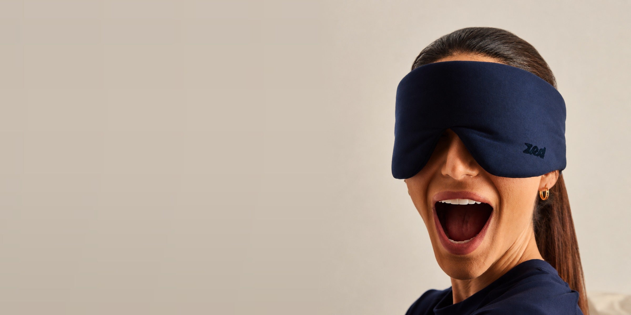 Woman wearing the navy Zed sleep mask over her eyes, laughing